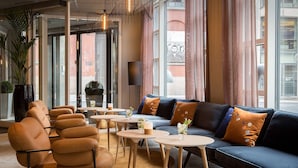 A modern lounge area with leather sofas, round tables, and a large window with curtains. - Scandic Victoria (Oslo)