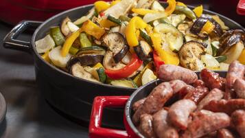 Un bufé con diversos platos, como papas al horno, verduras a la parrilla y salchichas.