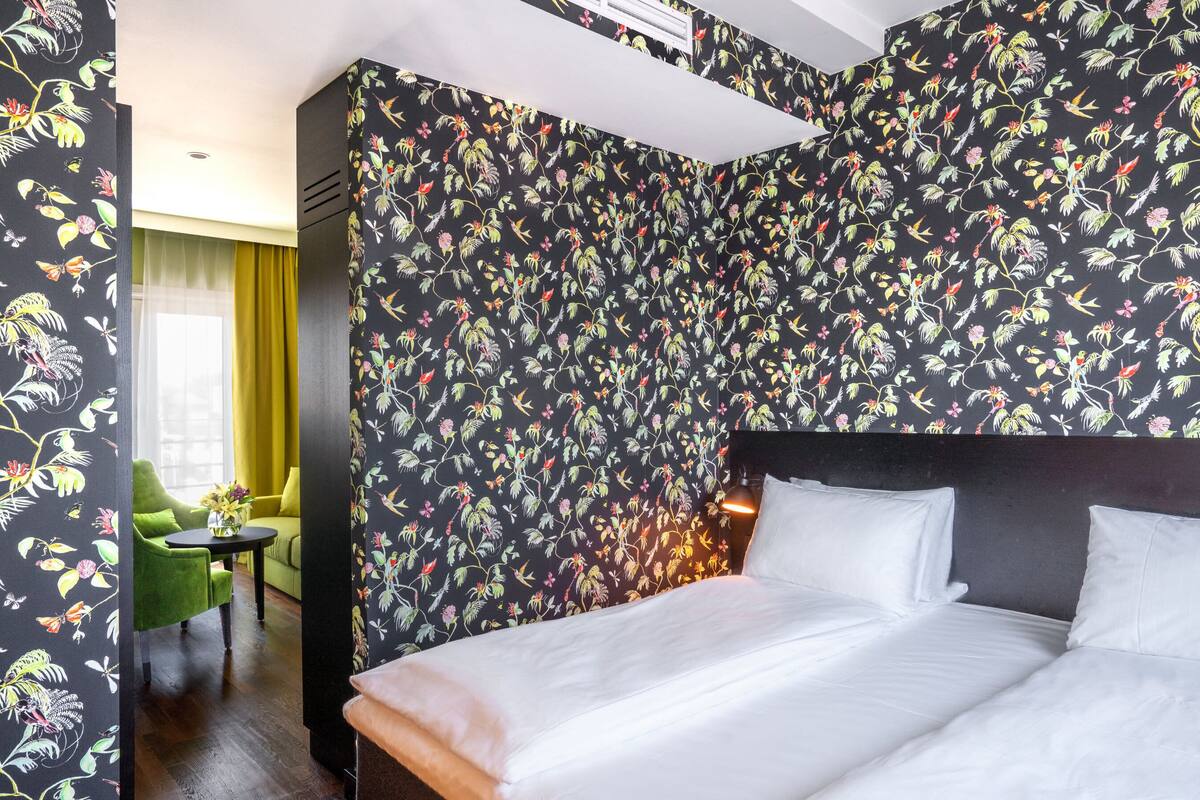 A hotel room with a large bed, a green armchair, and a small table with a vase of flowers.