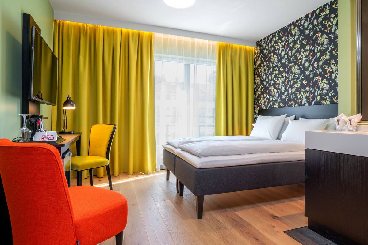 A hotel room with a bed, a desk with a lamp, a chair, and a bathroom area.