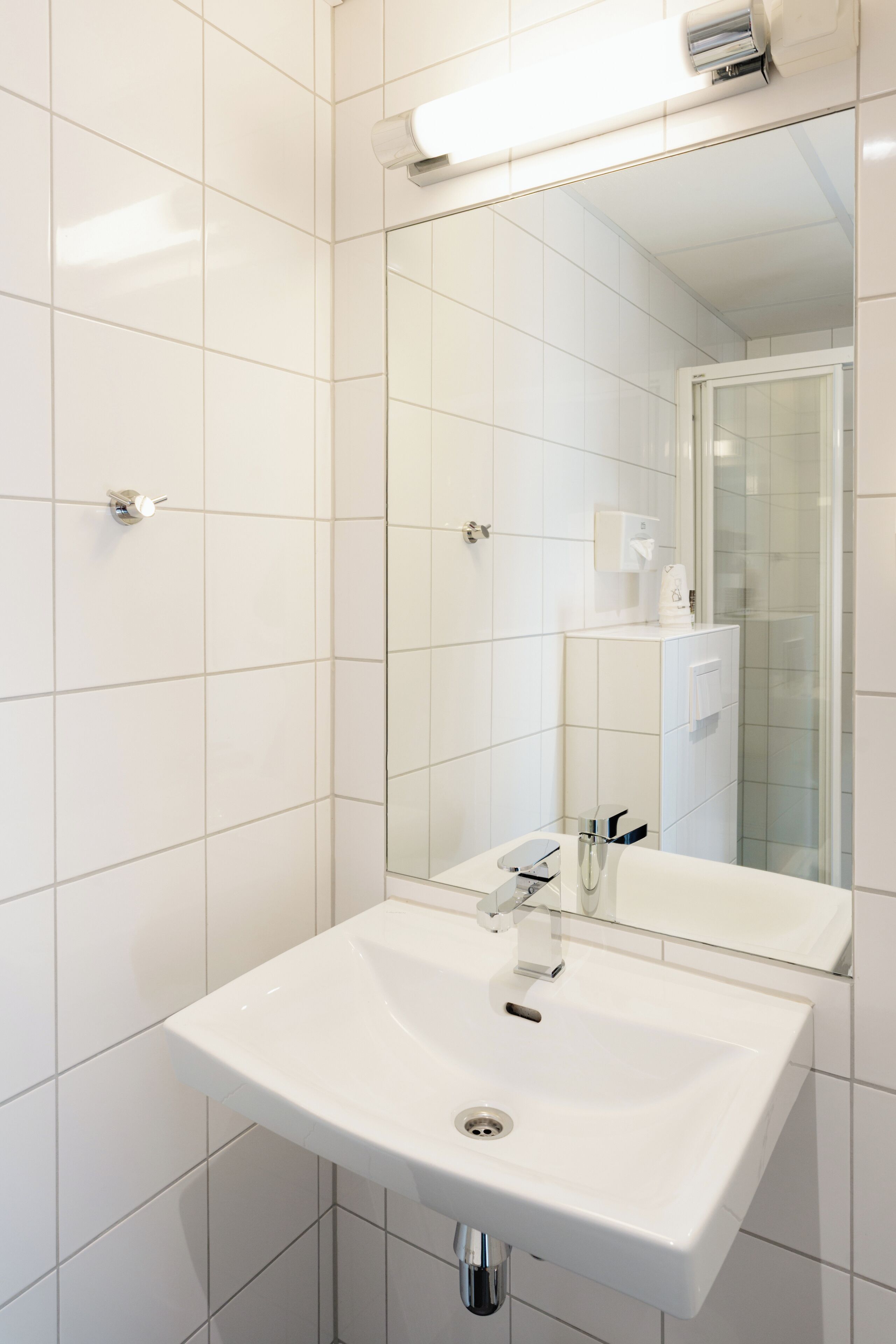 A modern bathroom with a white sink, mirror, and tiled walls.