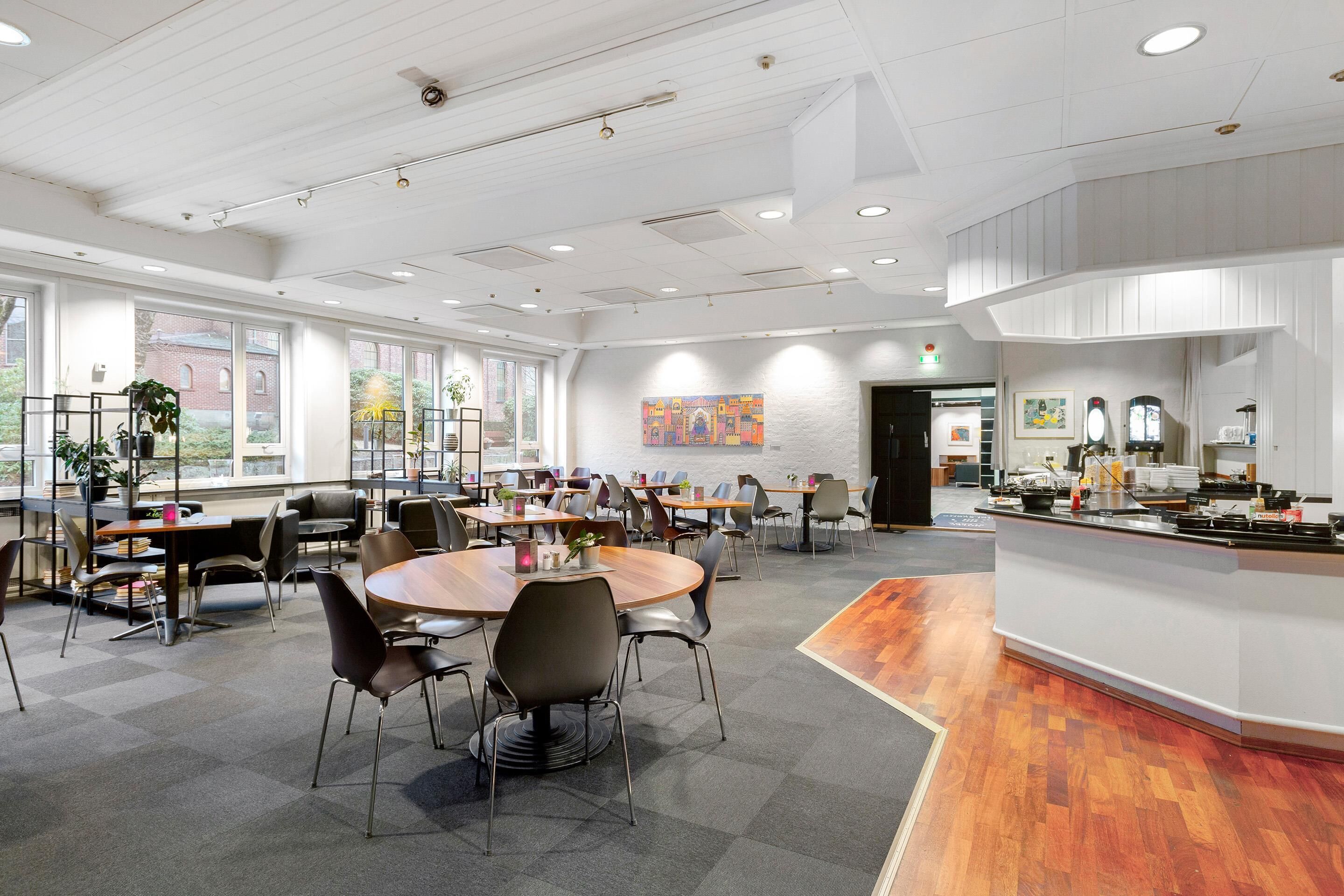 A spacious conference room with round tables, chairs, and a kitchenette area.
