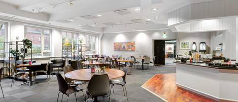 A spacious conference room with round tables, chairs, and a kitchenette area.