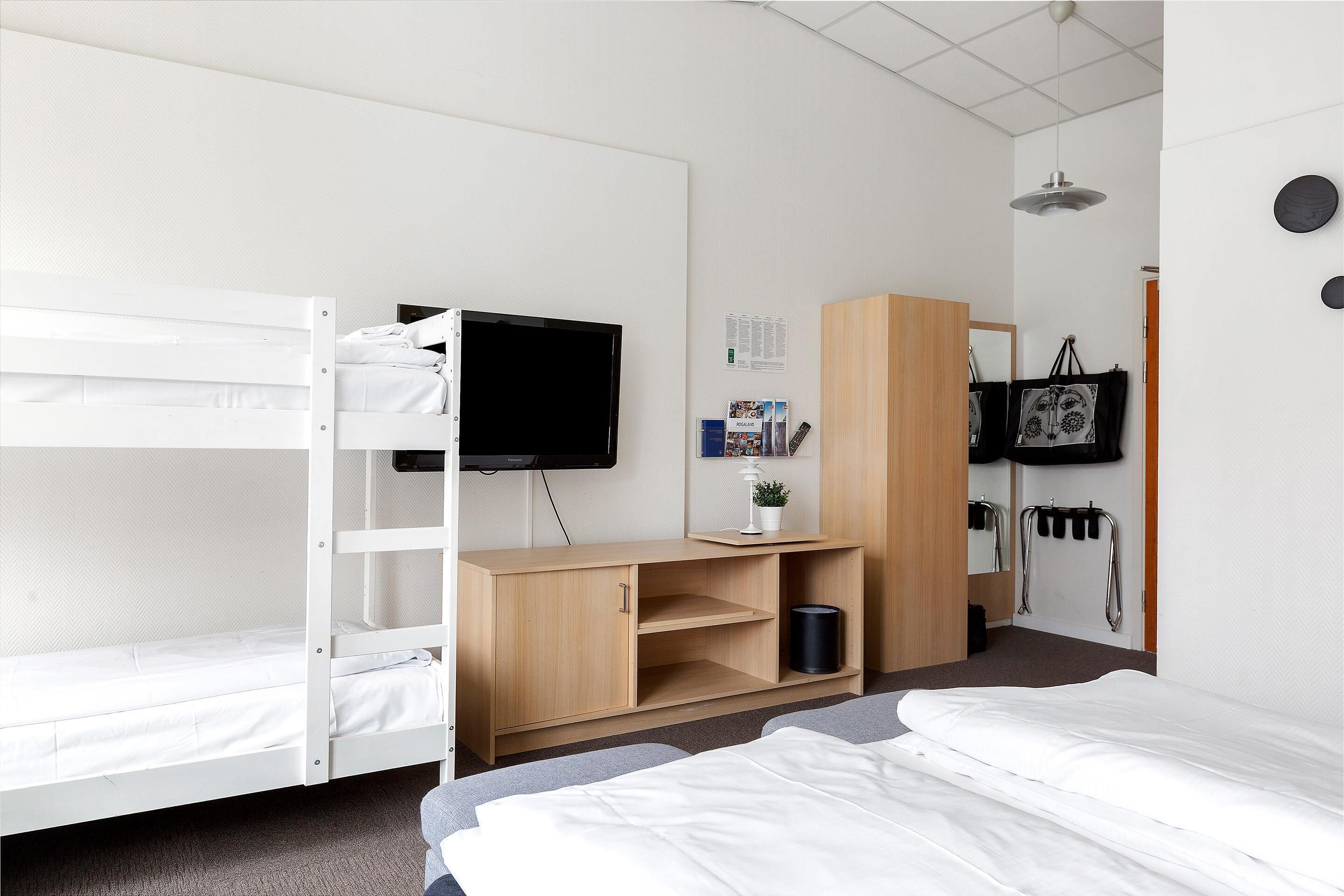A bunk bed room with a desk, a TV, and a wardrobe.