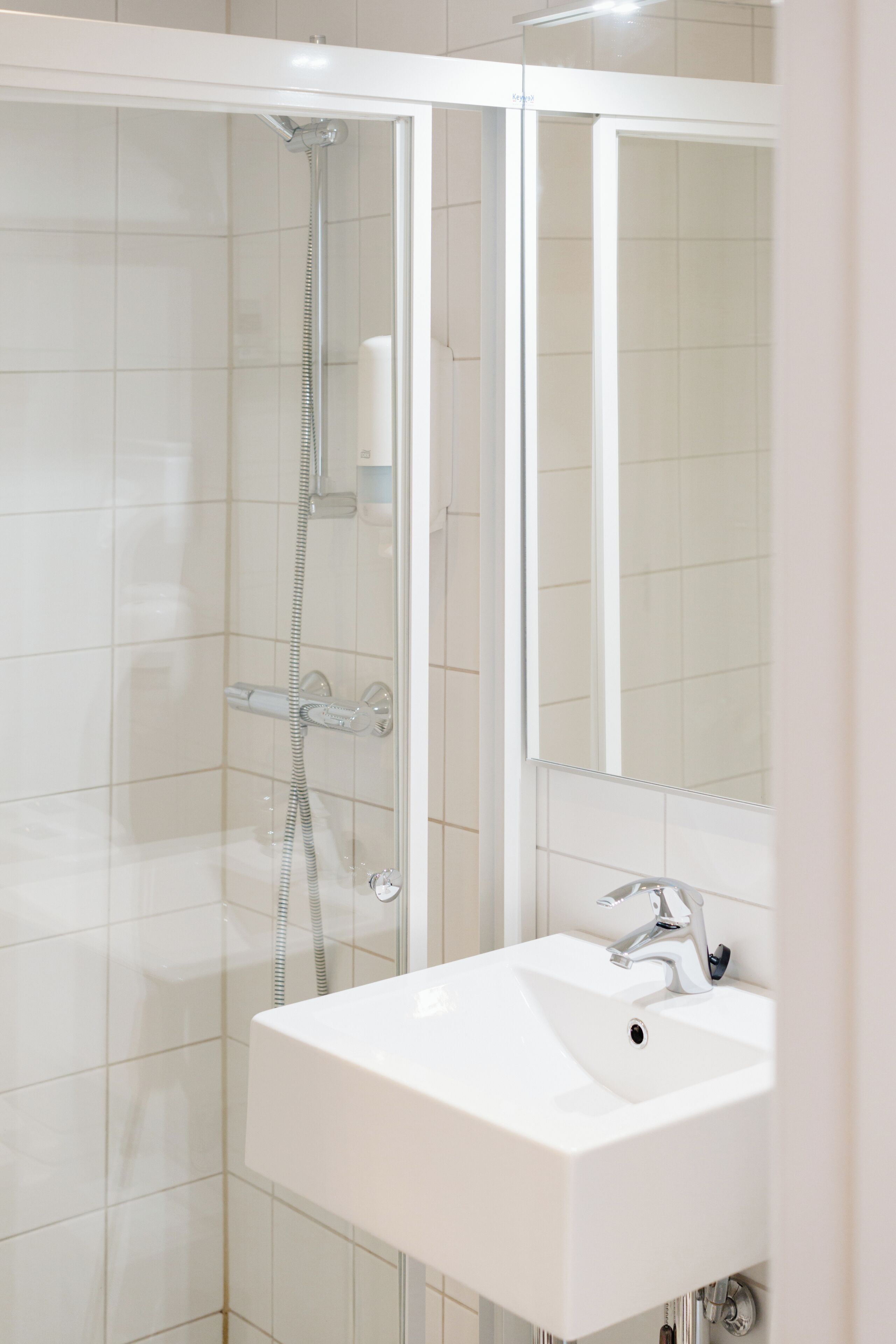A modern bathroom with a glass-enclosed shower, a white sink, and a mirror above the sink.