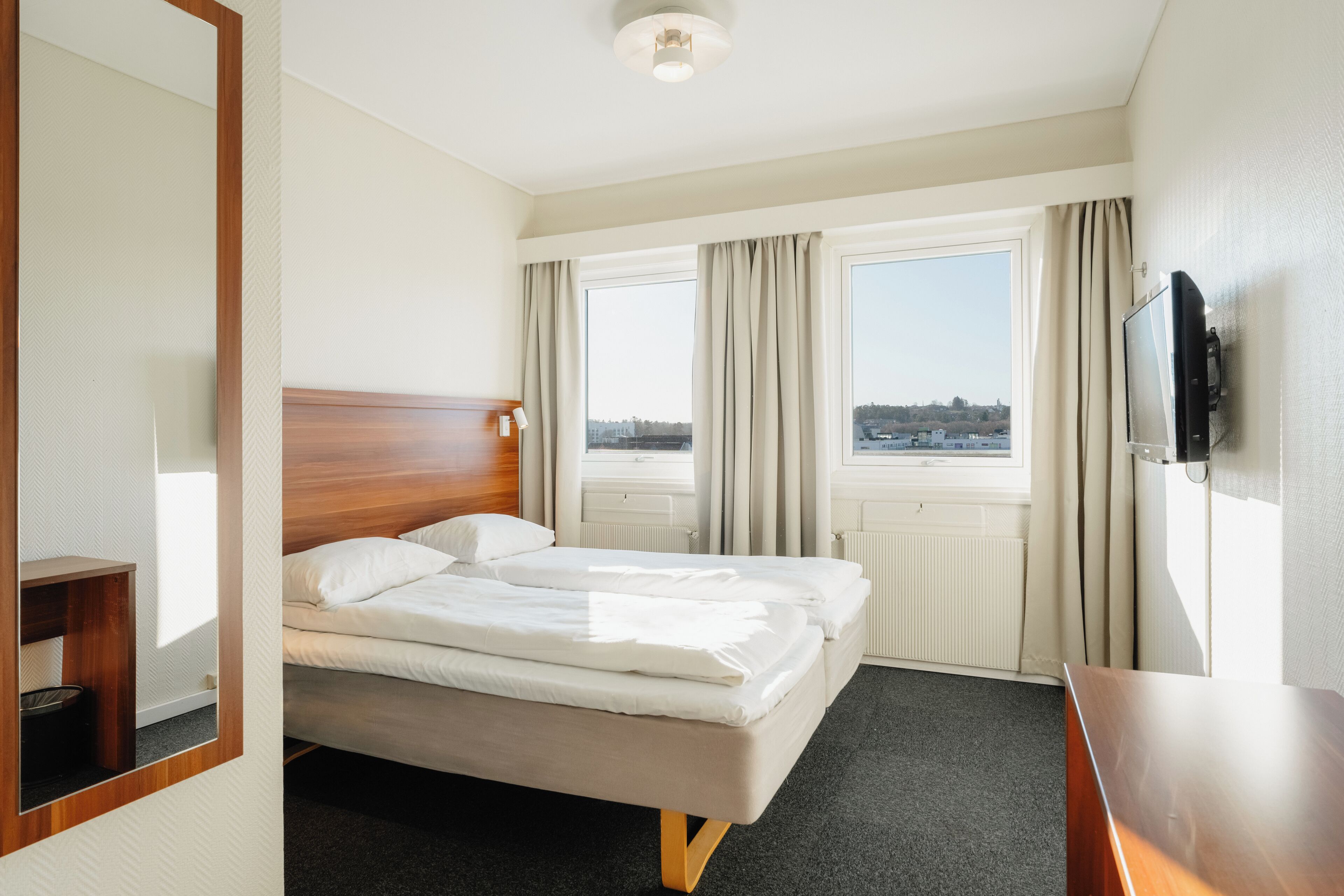 Une chambre d’hôtel avec un lit, une télévision, une fenêtre avec des rideaux et une vue sur la ville.