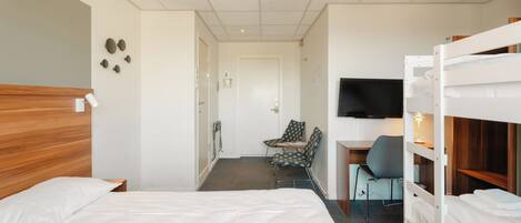 Habitación de hotel con literas, un escritorio con silla, televisor y puerta que da a un baño.