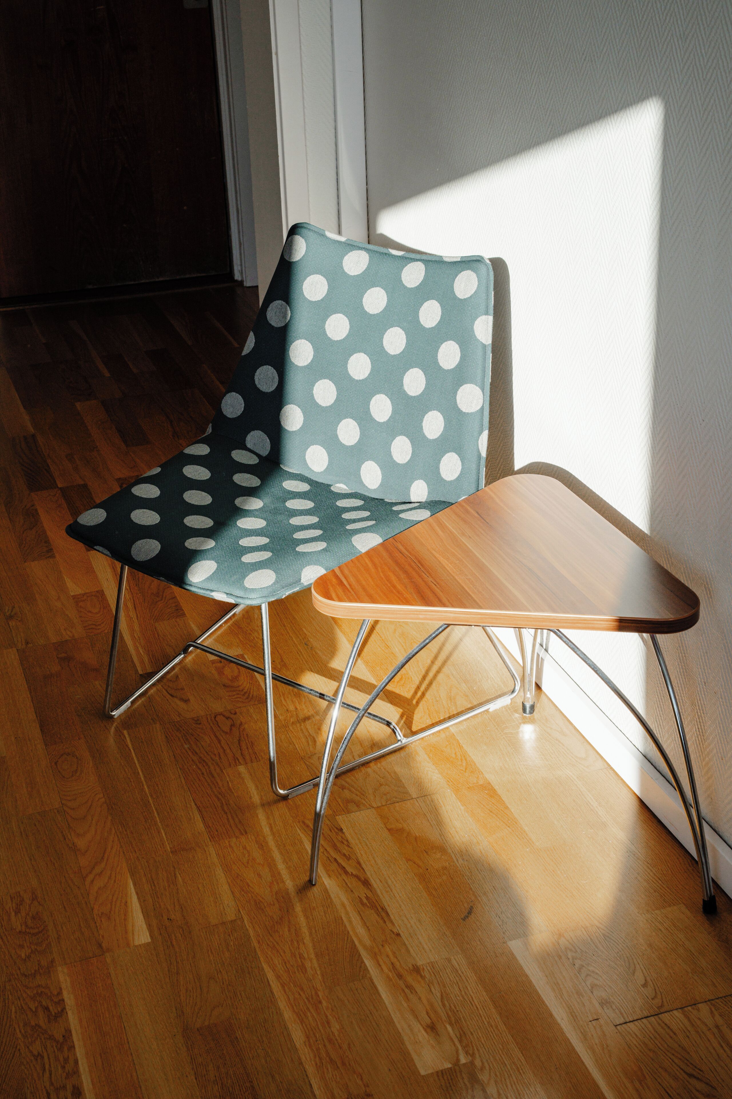 A chair with a teal cushion and white polka dots, a wooden table, and a wooden floor.