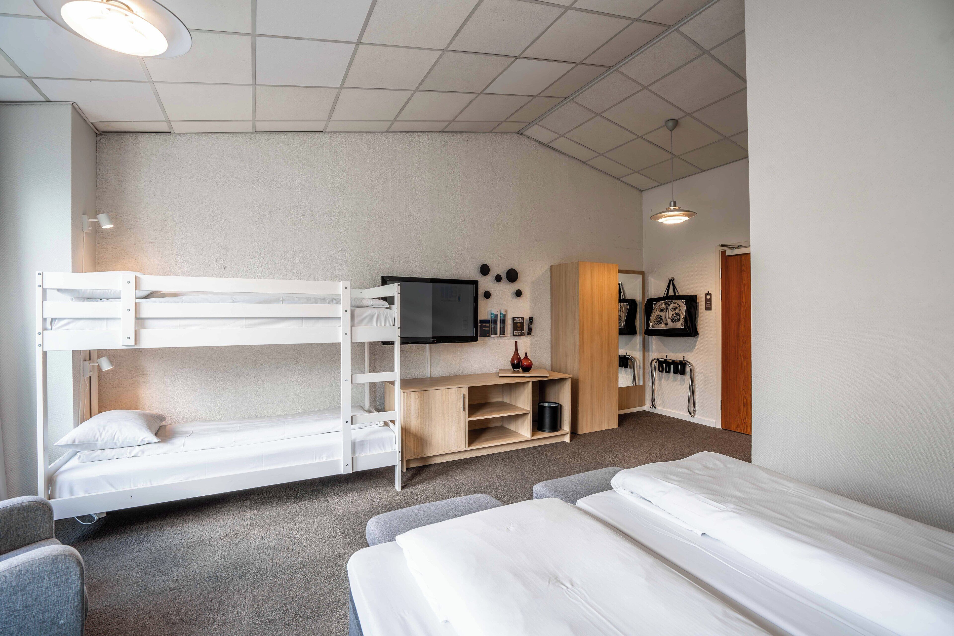A room with bunk beds, a television, a wooden cabinet, and a small seating area.