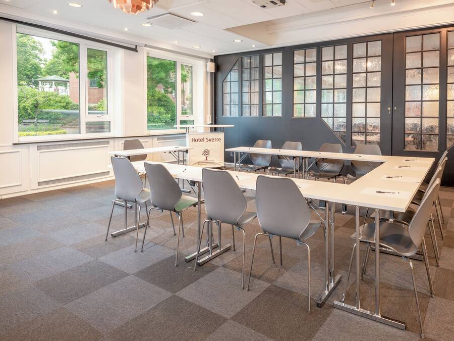 A conference room with a long table, grey chairs, and large windows with a view of greenery and buildings.