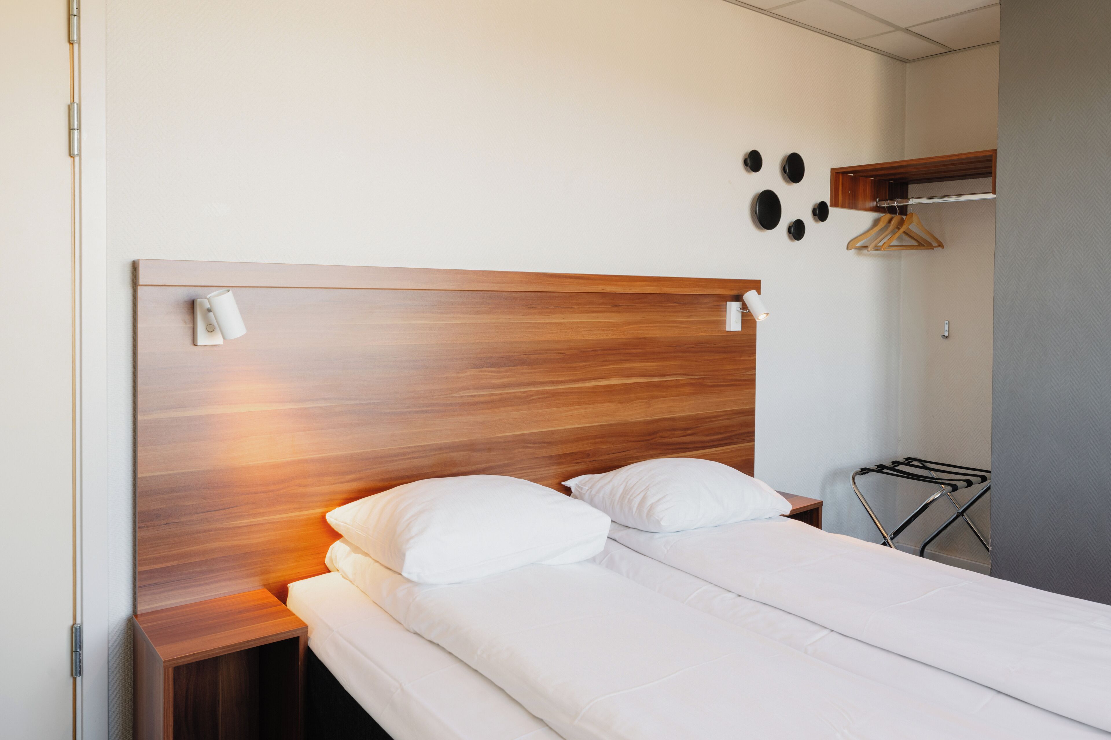 A neatly made bed with white linens, a wooden headboard, and a bedside table with a lamp.
