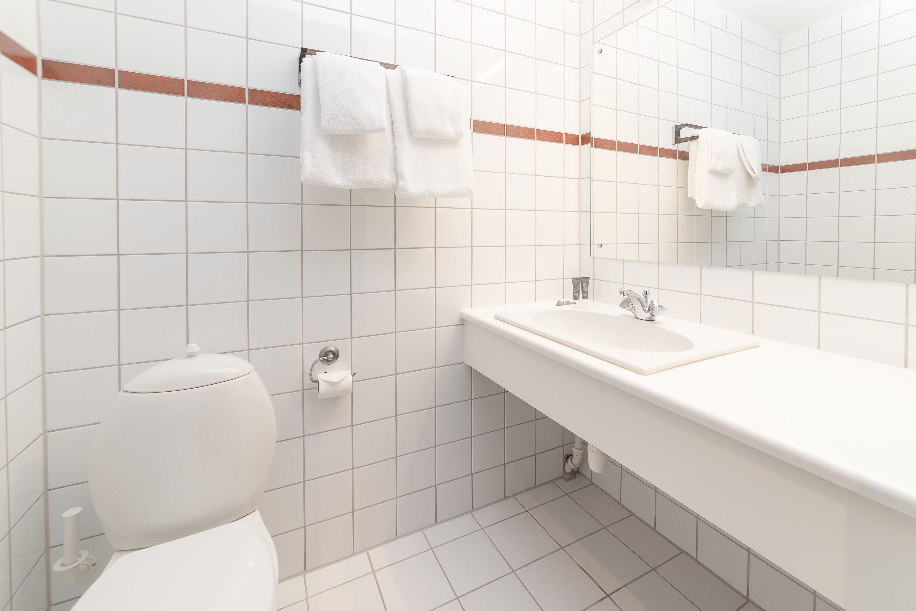 Un baño con inodoro, lavamanos y perchero para toallas.