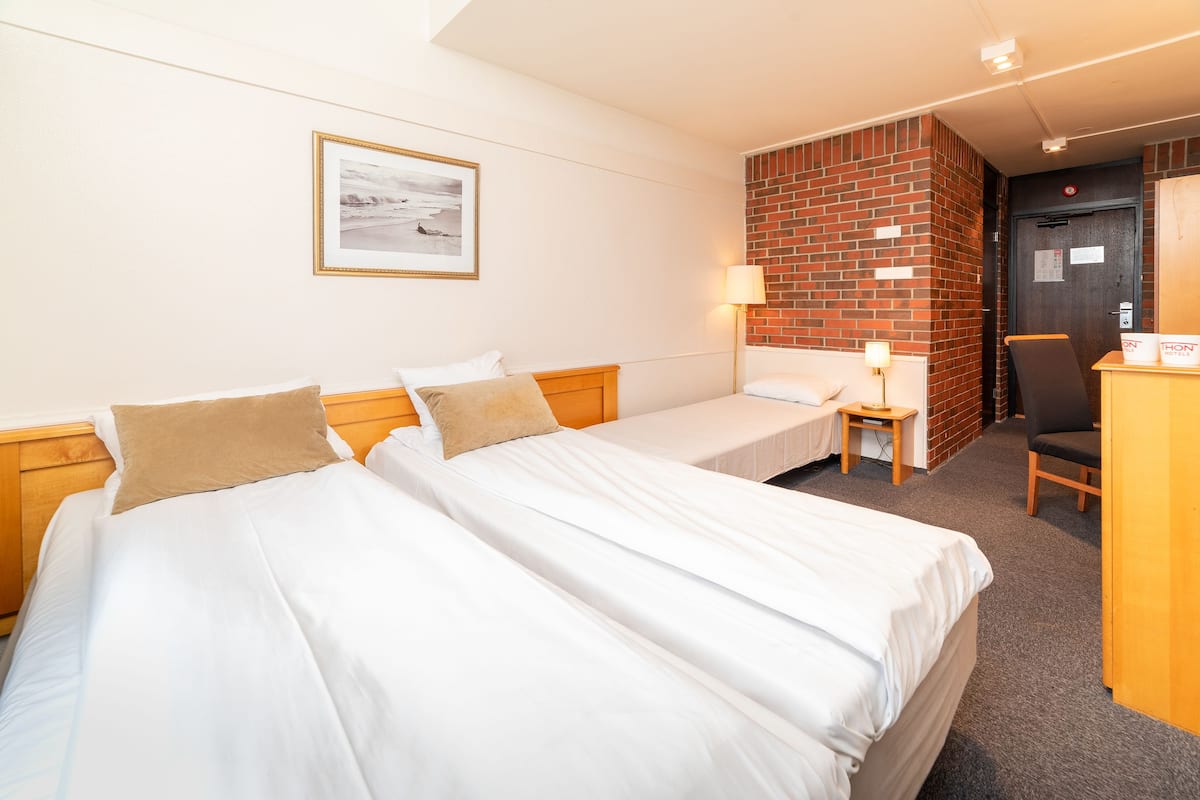 A hotel room with two beds, a desk, a chair, a lamp, and a framed picture on the wall.