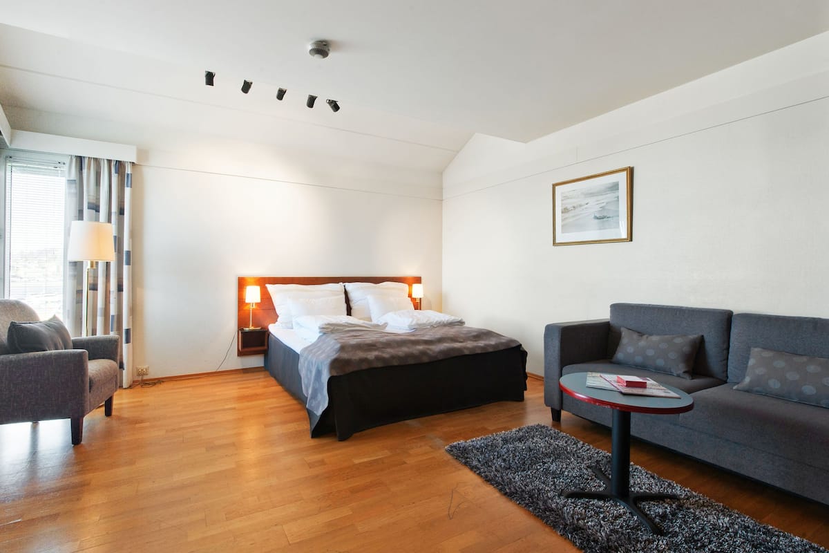 A hotel room with a bed, a sofa, a chair, a small table, and a picture on the wall.