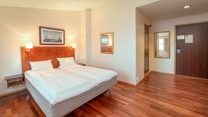 Una cama doble con cabecera de madera, dos mesitas de noche con lámparas y un cuadro enmarcado sobre la cama.