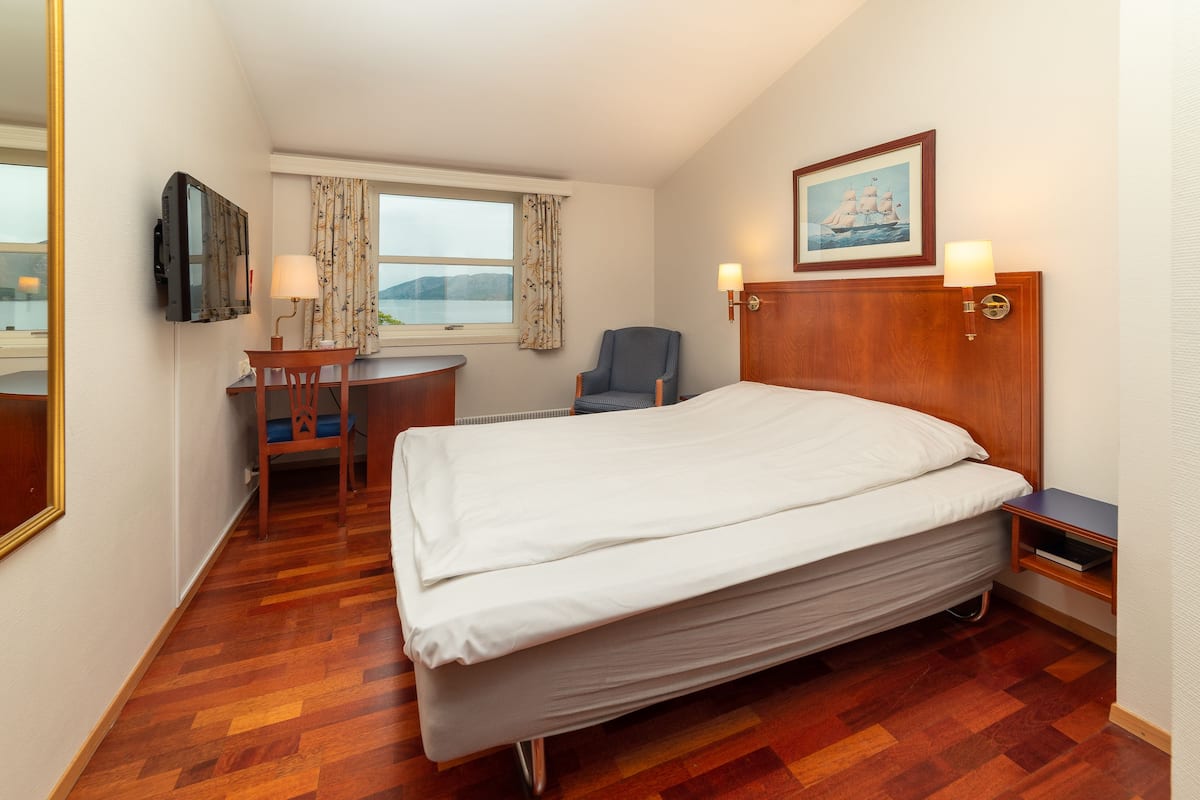 A hotel room with a bed, a desk, a chair, a TV, and a window with curtains.