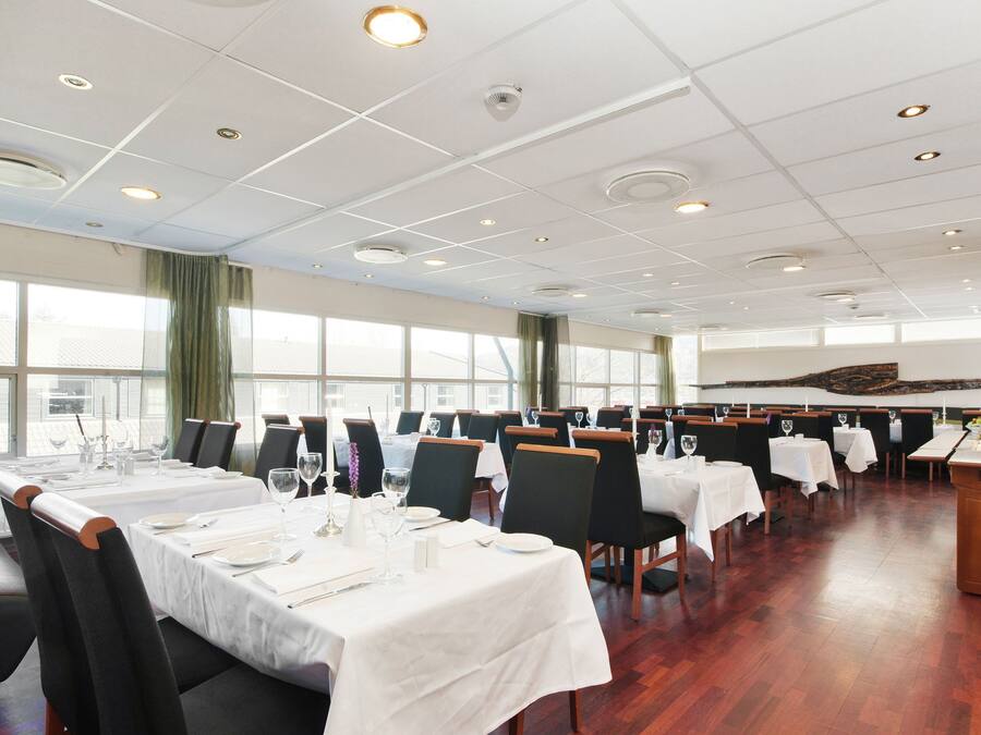 A spacious dining area with multiple tables set for dining, large windows providing natural light, and a modern ceiling design.