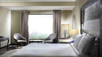 A hotel room with a bed, two chairs, a desk, a lamp, and a large window with curtains.