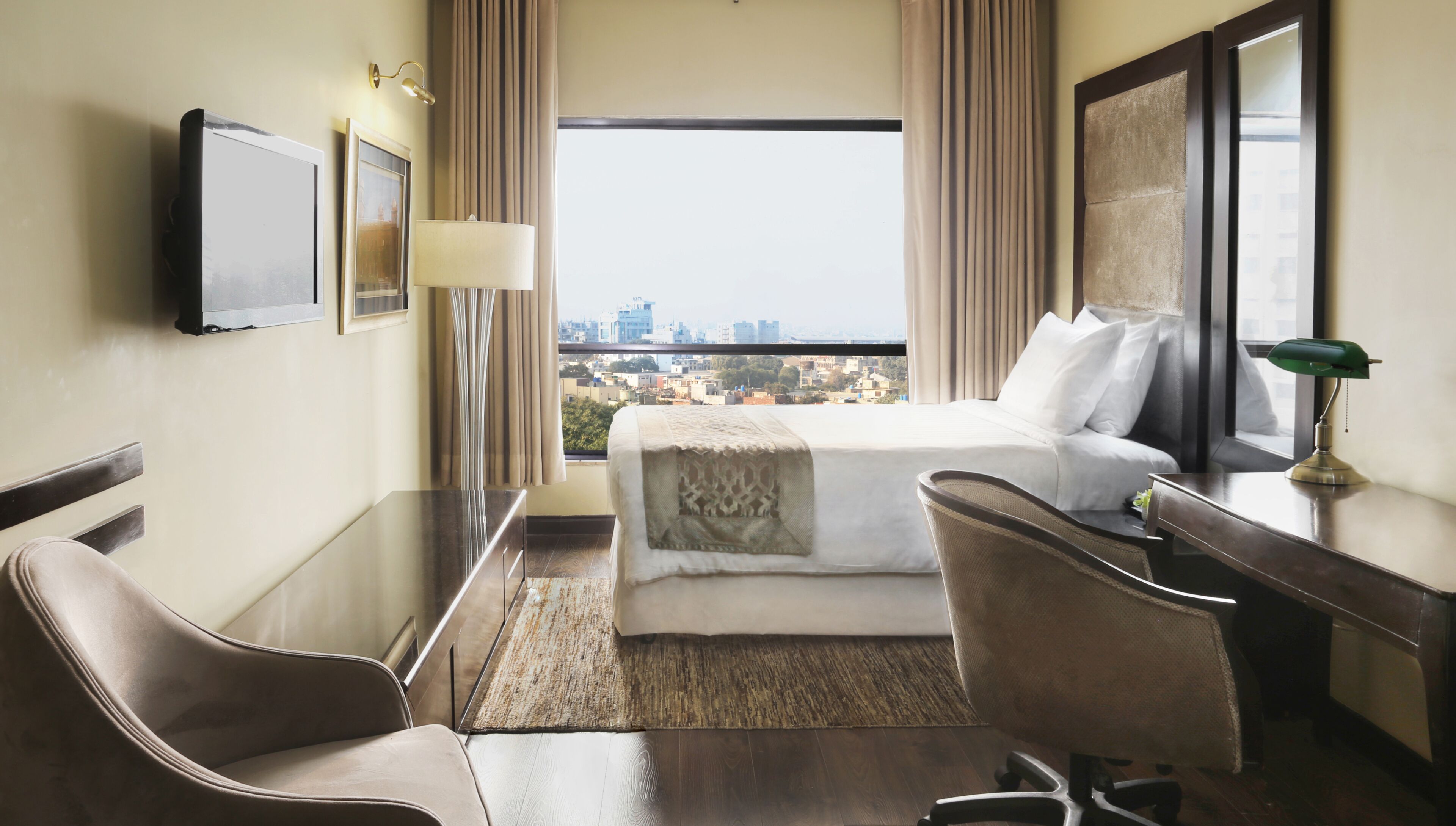 Habitación de hotel con cama, escritorio, silla y vista a la ciudad.
