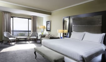 Habitación de hotel con una cama grande, dos sillones, una mesita, un sofá, un ventanal amplio y un espejo.