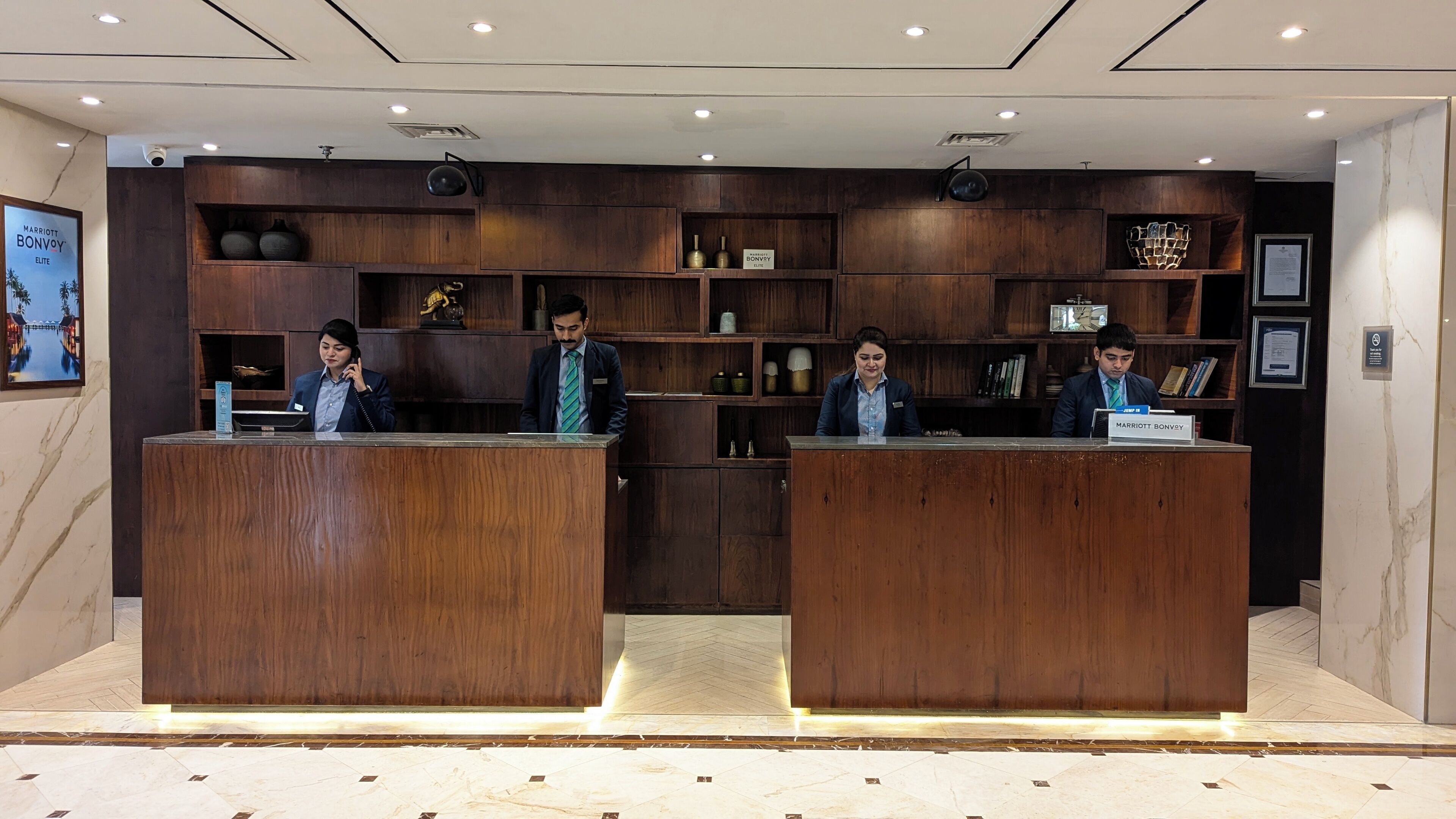 A hotel reception desk with wooden paneling and a marble floor.