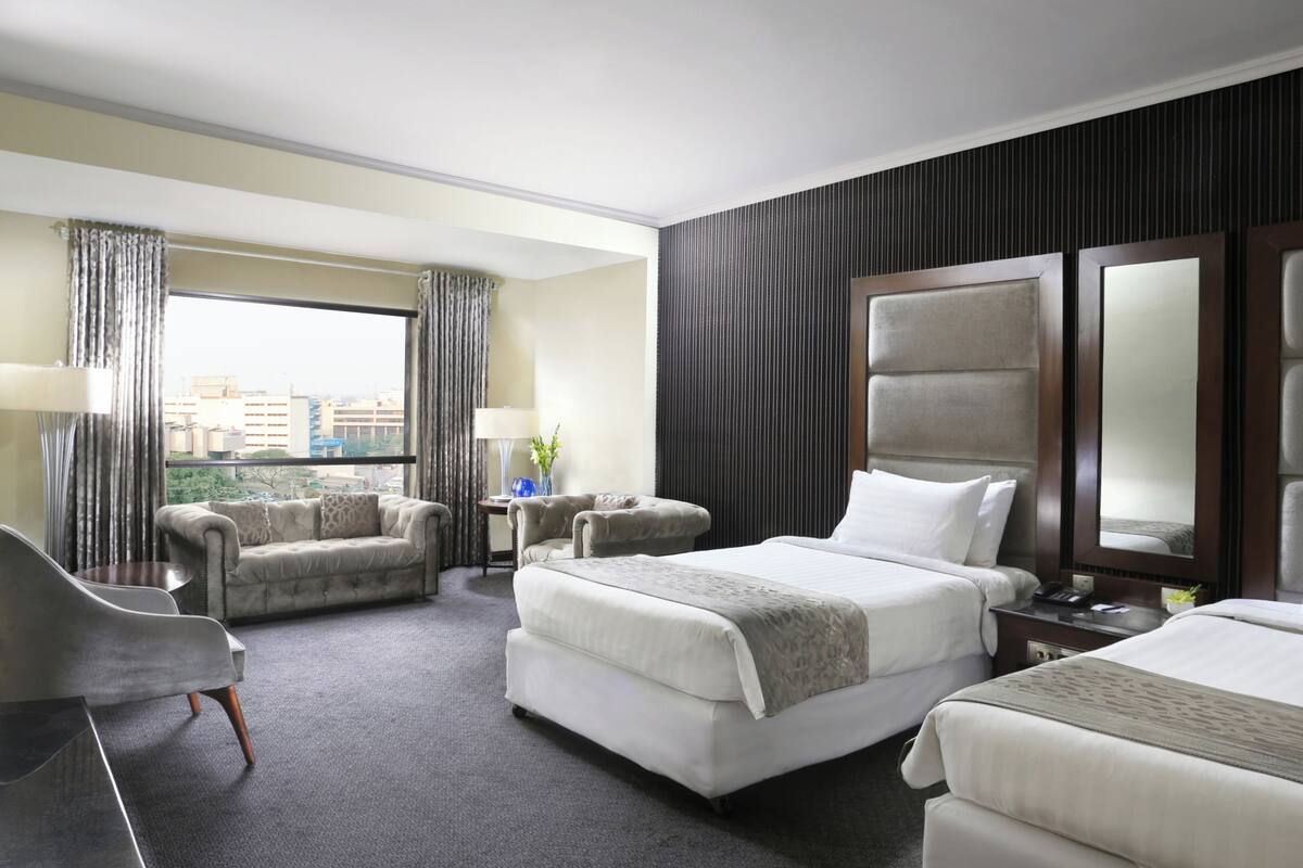 A hotel room with two beds, a sofa, a desk, and a view of the city.