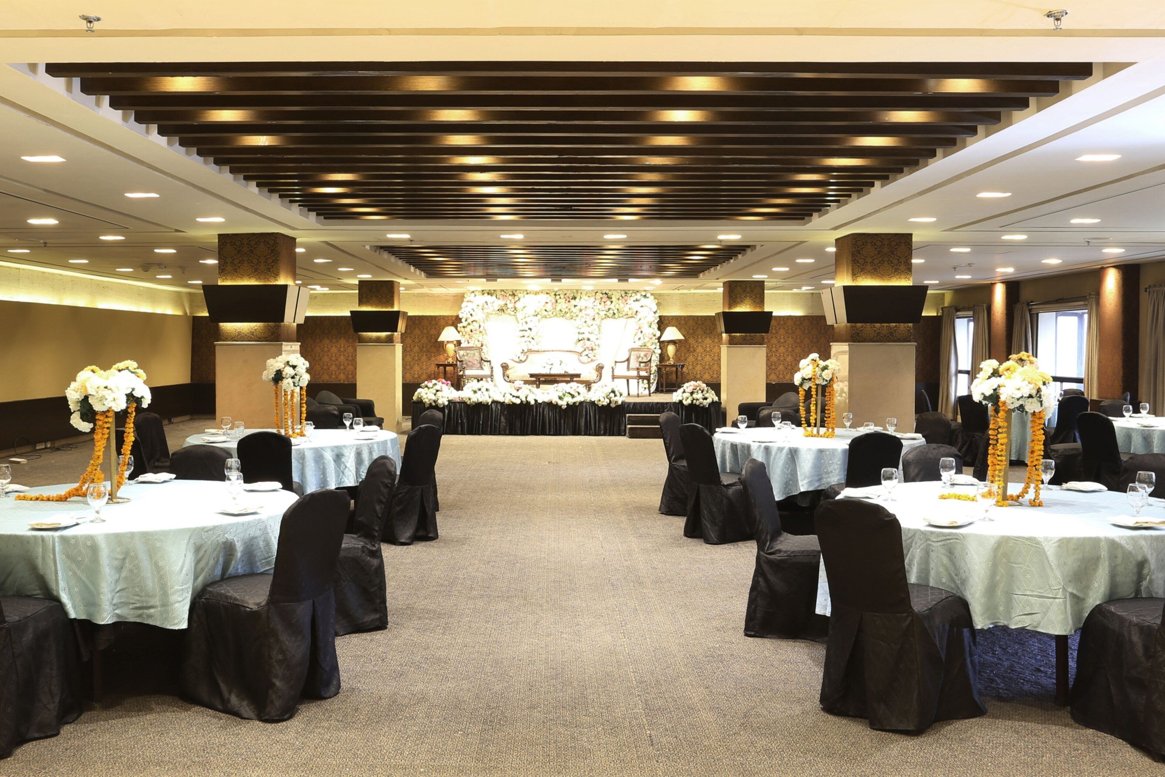 A banquet hall with round tables, black chairs, and floral centerpieces.