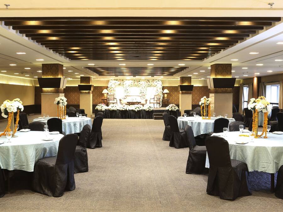 A banquet hall with round tables, black chairs, and floral centerpieces.