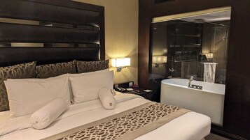 A hotel room with a bed, a nightstand, a lamp, a bathroom with a bathtub, and a mirror.