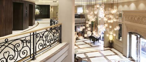 A grand hotel lobby with a marble floor, a curved staircase, and a decorative light fixture.