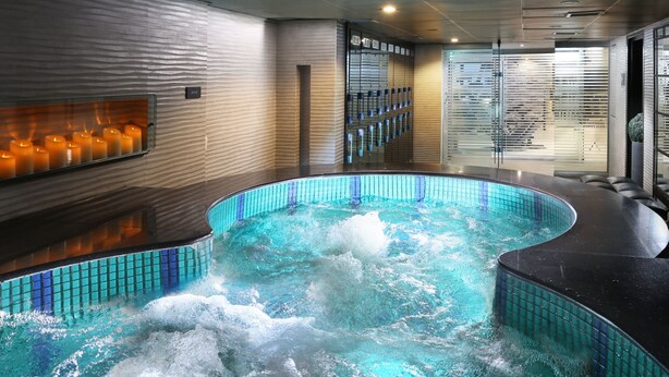 A modern indoor swimming pool with a curved design, surrounded by a tiled wall and a seating area. - Four Points by Sheraton Lahore (Lahore)