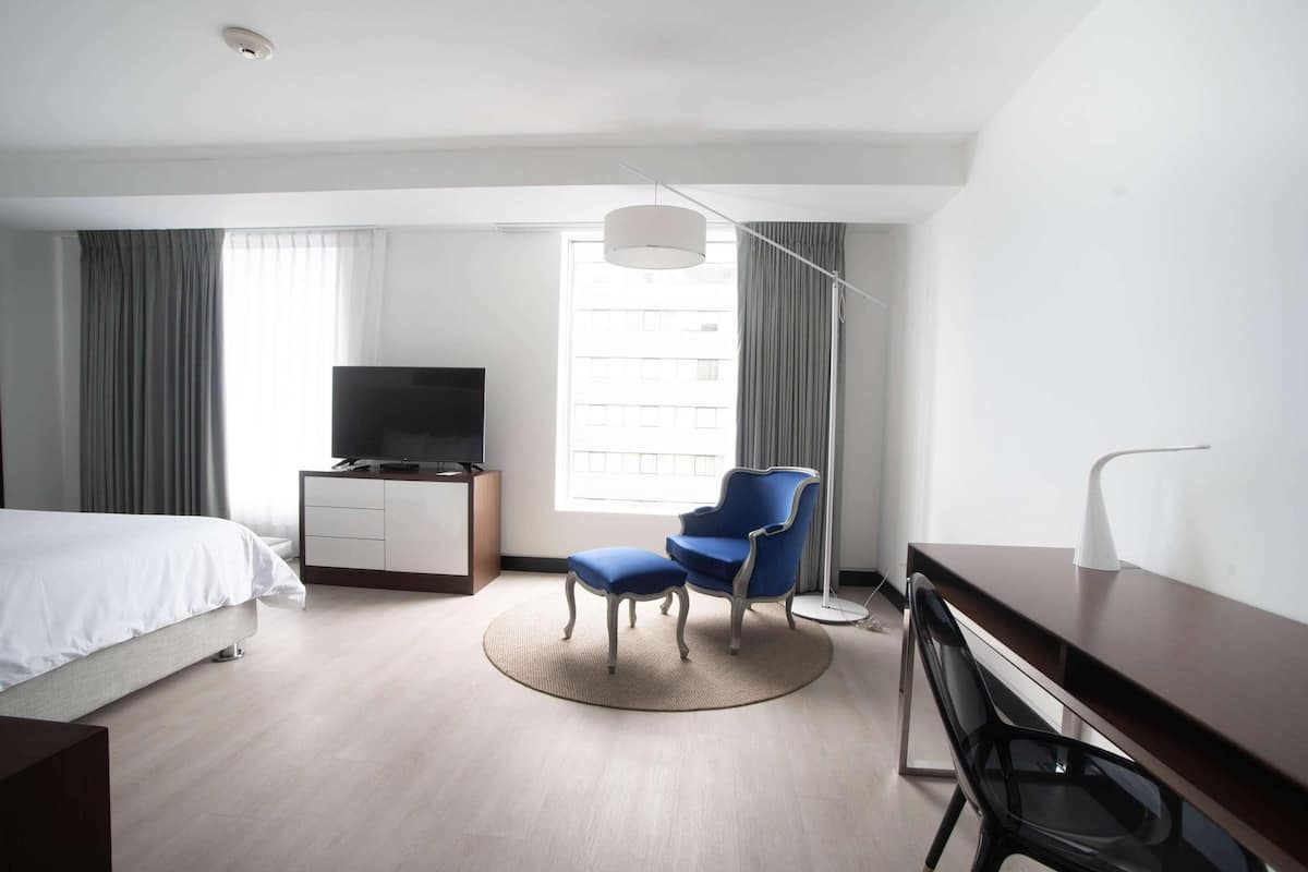 A hotel room with a bed, a desk, a chair, a television, and a large window with curtains.