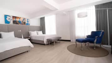Ein Hotelzimmer mit zwei Betten, einer Bank, einem blauen Sessel und einem großen Fenster mit Vorhängen.