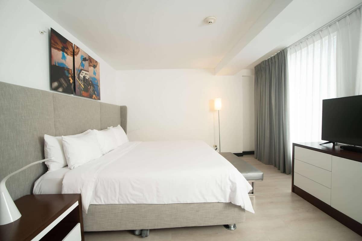 A modern hotel room with a large bed, a bedside table with a lamp, a TV, and a painting on the wall.