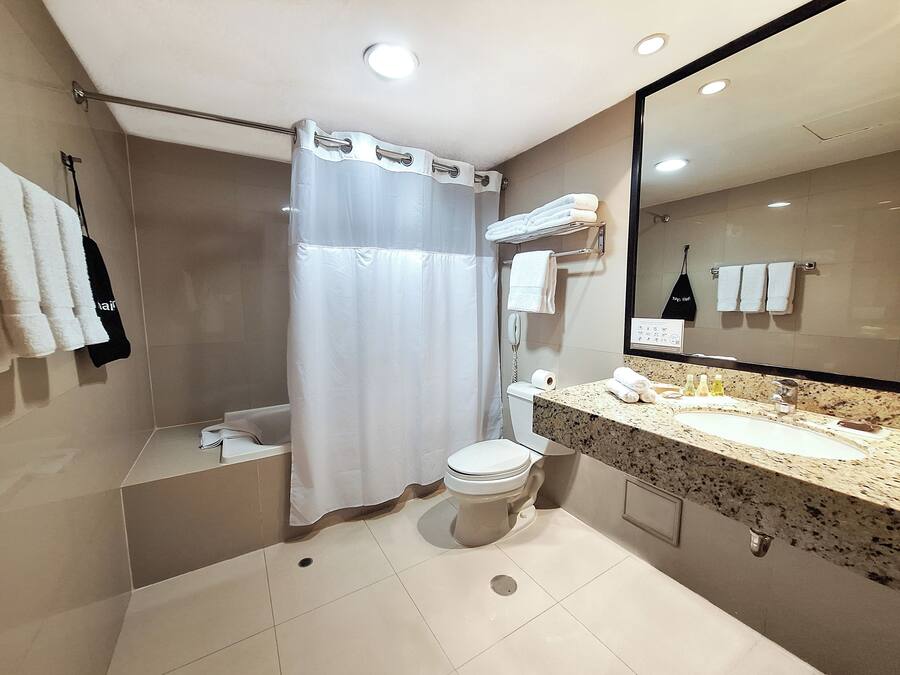 Un baño moderno con cortina de ducha, inodoro, lavamanos con espejo y varias toallas colgadas en la pared.