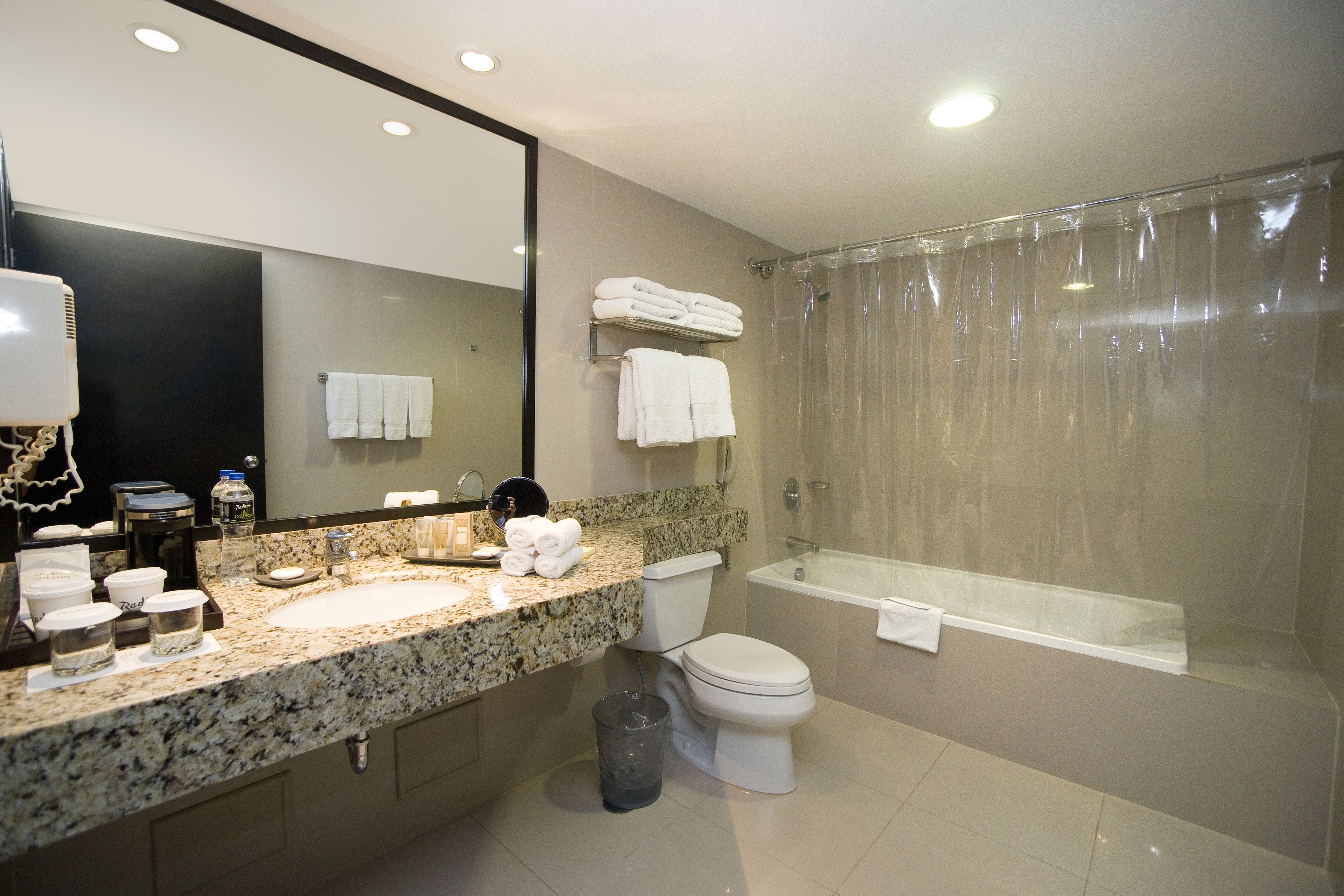A modern bathroom with a granite countertop, a toilet, a bathtub, and a glass shower enclosure.