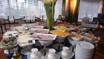 A buffet with various food items and beverages, arranged on tables in a well-lit room with large windows.