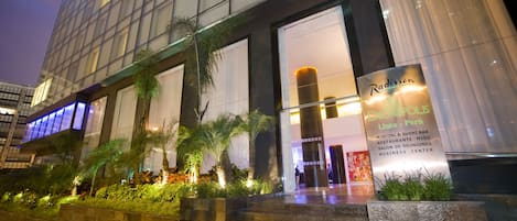 A modern building with a glass facade, a sign for Radisson Lima - Peru, and a well-lit entrance with steps leading up to it.