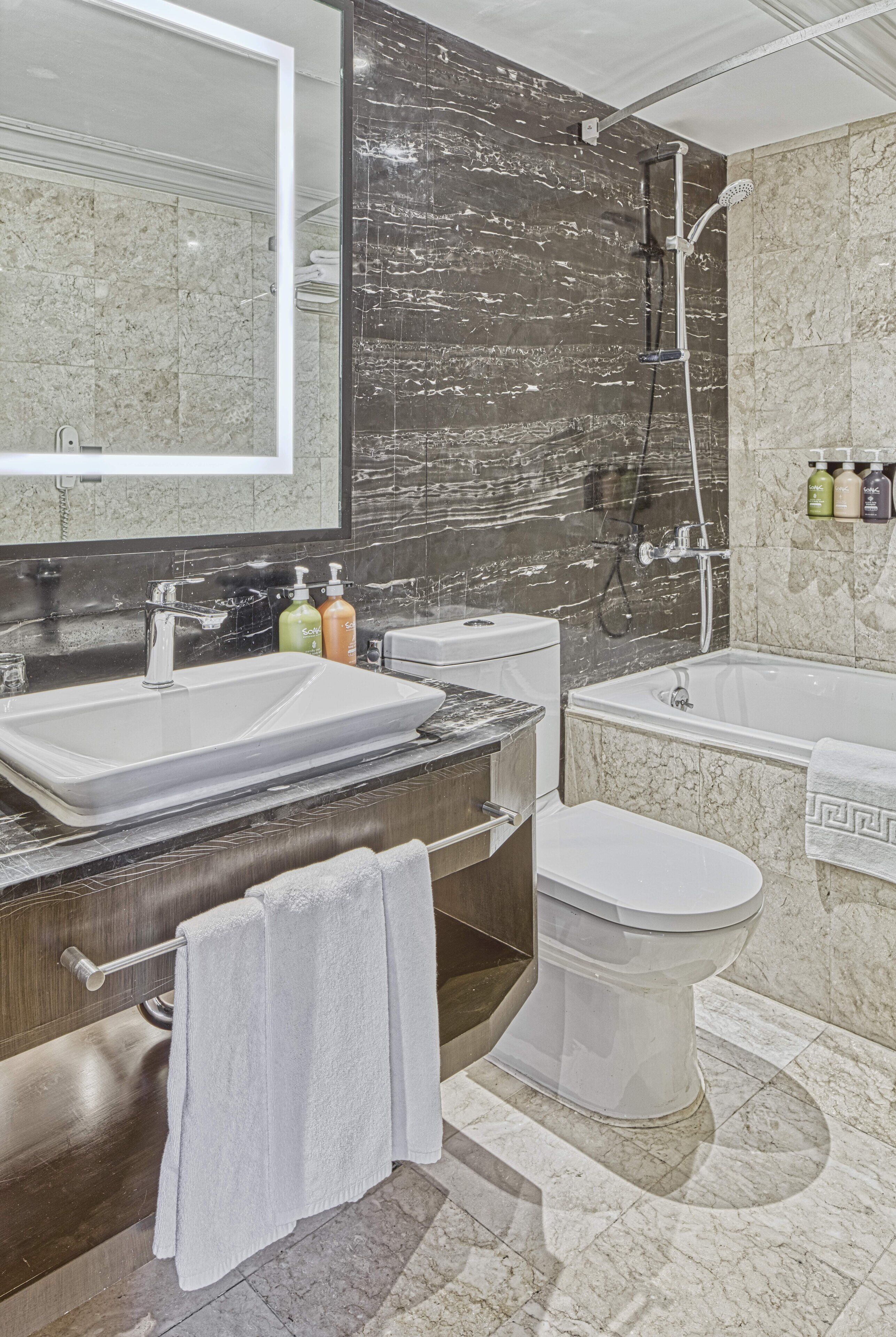 A modern bathroom with a large mirror, two sinks, a toilet, and a bathtub.