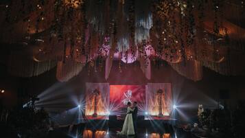 A wedding ceremony with a couple on stage, surrounded by draped floral arrangements and a backdrop with a snowflake design.
