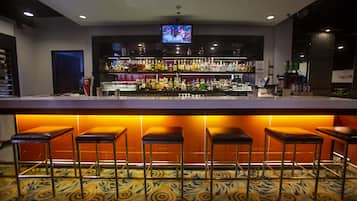 A bar area with a television screen, multiple shelves of bottles, and bar stools.
