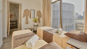 Ein Hotelzimmer mit zwei Betten, einem großen Fenster mit Blick auf die Stadt, einem Spiegel und einem kleinen Tisch mit einer Vase.