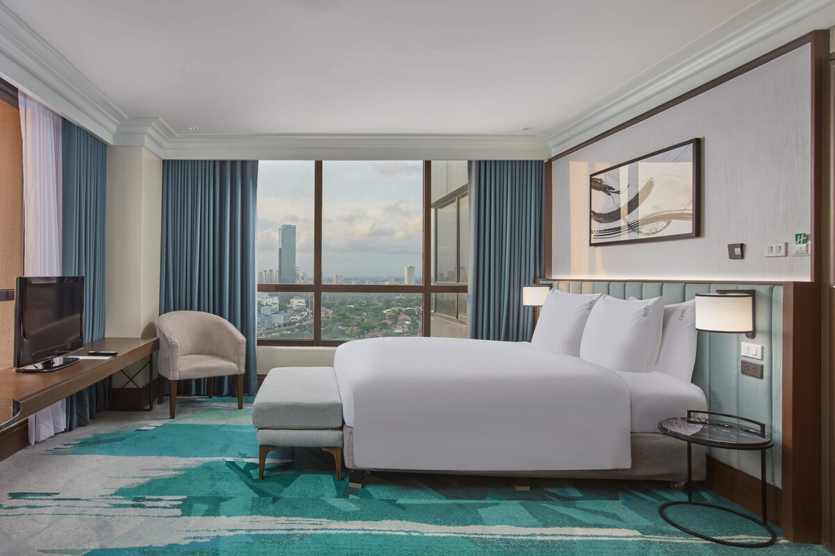 Une chambre d’hôtel avec un grand lit, un bureau avec une télévision, une chaise, une petite table et une vue sur la ville.