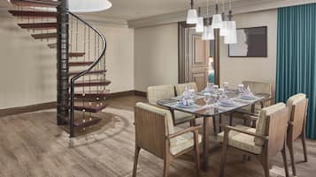 Een eetgedeelte met een houten tafel voor zes personen, omringd door gestoffeerde stoelen, een spiltrap en hanglampen.