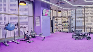 A gym with purple walls, exercise equipment, and a view of buildings through large windows.