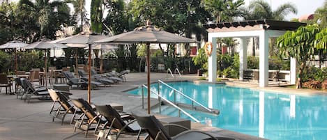 A poolside area with lounge chairs and umbrellas, surrounded by palm trees and a clear blue pool.