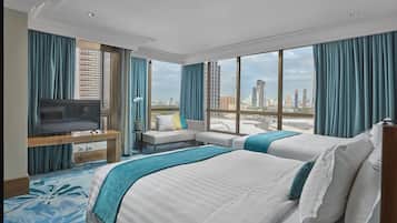 A hotel room with two beds, a TV, a sofa, and a large window with a city view.