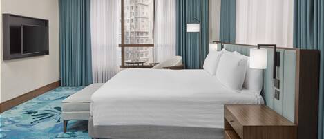 Hotelkamer met een groot bed, een aan de muur bevestigde televisie, een tafeltje met stoelen en uitzicht op de stad.