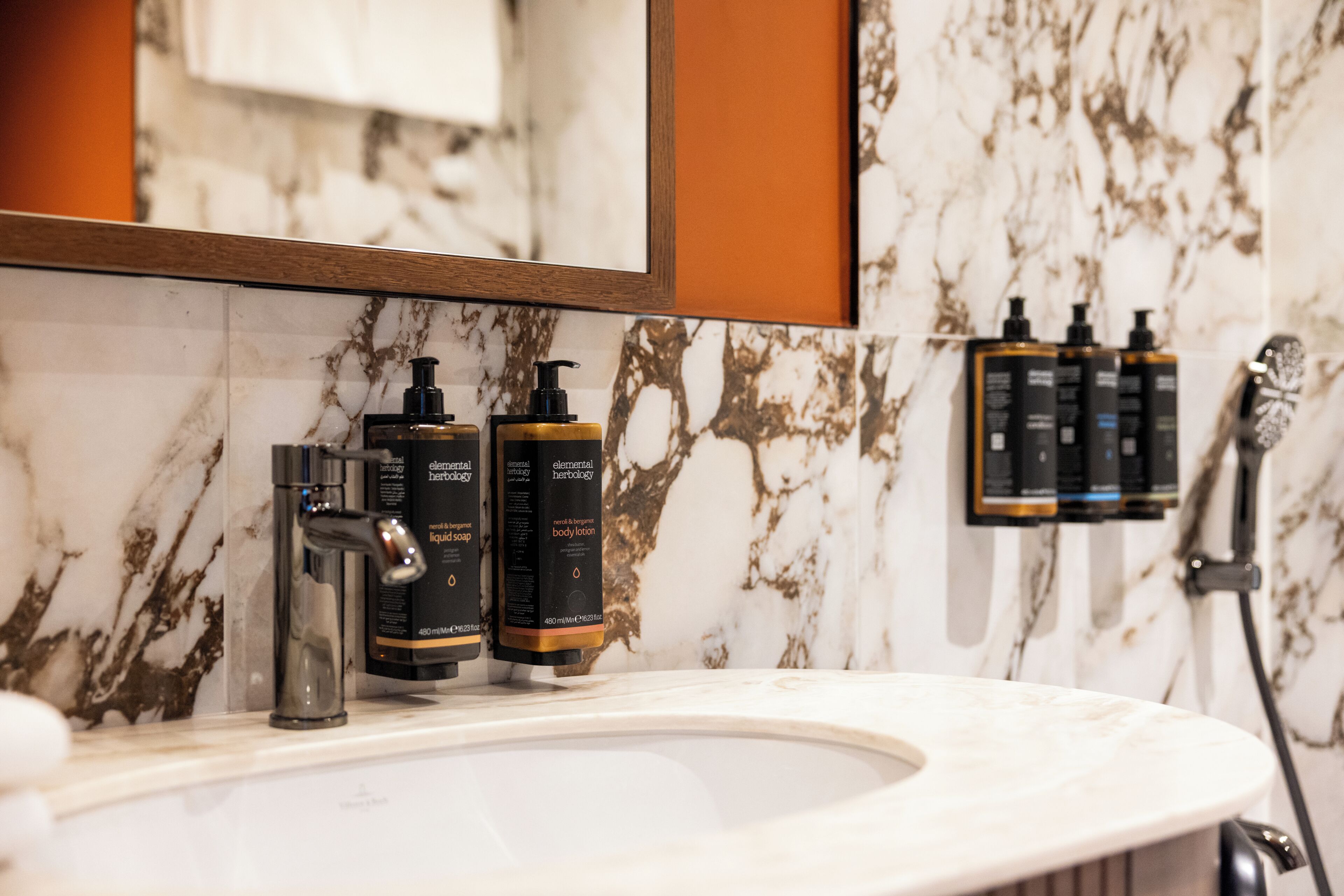 A bathroom with a marble sink, a mirror, and toiletries on the wall.