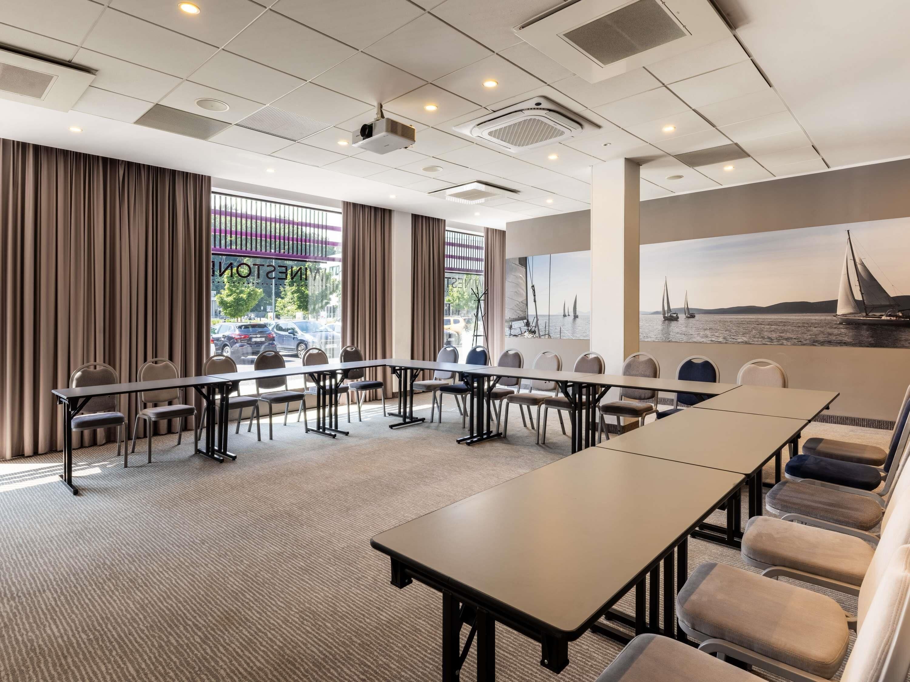 Un salón de conferencias con una larga mesa, sillas, un proyector y ventanas amplias con vista a veleros.